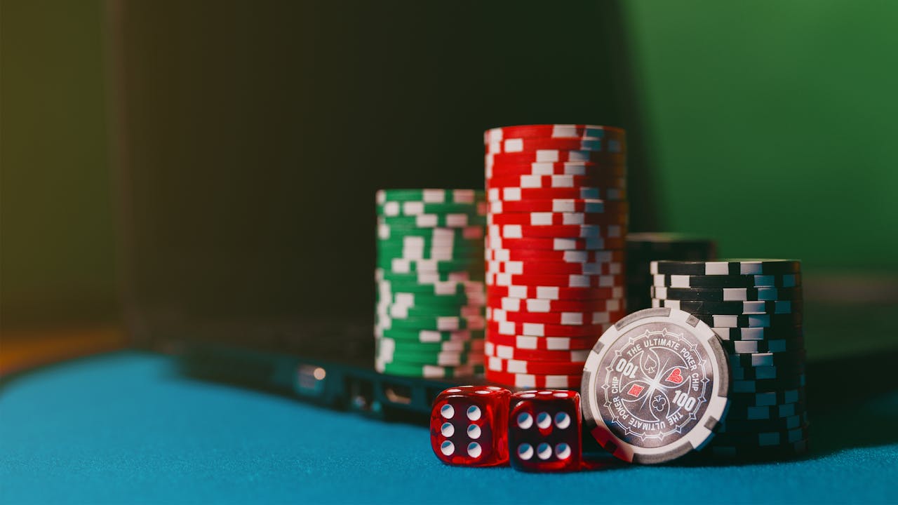 home-hero Close-up of casino chips and dice on a felt table, next to a laptop for online gambling.